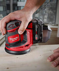 Slick Cordless Random Orbit Sander Kit With M18 Battery Pack for smooth wood finishing in use on flat surface.