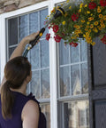 Person using Relax Grip 15 Inch Garden Hose Wand With 8 Pattern Sprayer And Easy Thumb Control Adaptor Arthritis Friendly Lightweight Watering Wand For Lawn Garden And Patio to water hanging flowers.