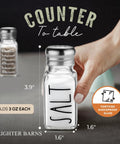 Hand holding Clear Glass Salt And Pepper Shaker Set With Stainless Steel Lids For Modern Farmhouse Kitchen Decor Perfect For Home.