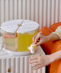 Five Point Five Liter Rotating Beverage Dispenser With Four Separate Compartments And Dripless Spigot, serving yellow drink.