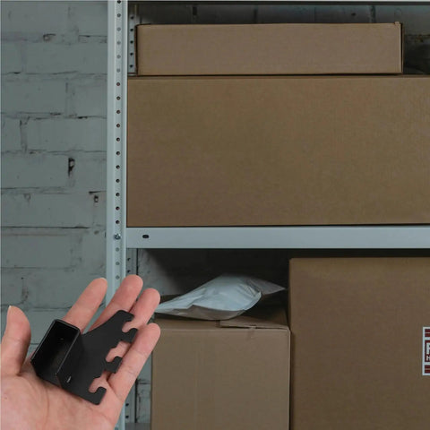 Hand holding Beefy Heavy Duty Stainless Steel Square Pipe Shelf Bracket with boxes in background