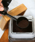 Hand holding EZ Scoop Coffee Scooper And Funnel For Reusable K Cup Pods, Two Tablespoon Capacity over coffee jar