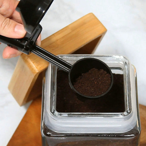 Hand holding EZ Scoop Coffee Scooper And Funnel For Reusable K Cup Pods, Two Tablespoon Capacity over coffee jar