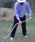 Person using a Curved Metal Scythe Blade And Snath With A 53 Inch Handle 22 And A Half Inch Long Blade By 2 And A Quarter Inch Wide Reinforced Spine Made In USA Handcrafted For Light Brush Clearing Grass And Grain Work outdoors