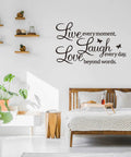 Live Every Moment Laugh Every Day Love Beyond Words Wall Sticker on a bedroom wall above a wooden bed with decor elements.