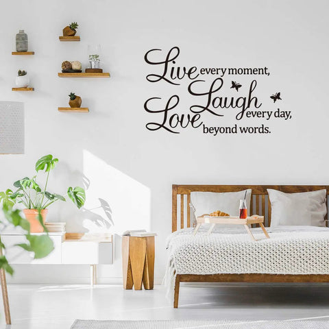 Live Every Moment Laugh Every Day Love Beyond Words Wall Sticker on a bedroom wall above a wooden bed with decor elements.