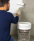 Man applying Super Slick Basement Sealer White 5 Gallon on concrete wall using a roller, showcasing waterproofing application.
