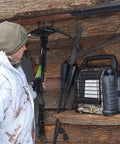 Person in winter gear with crossbow near 12,000 BTU portable propane radiant heater for camping and hunting, camouflage finish