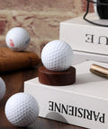 Wooden Golf Ball Display Stand For Desk With 2 Inch Ball Holder showcasing a golf ball on a tabletop with books and pen nearby.