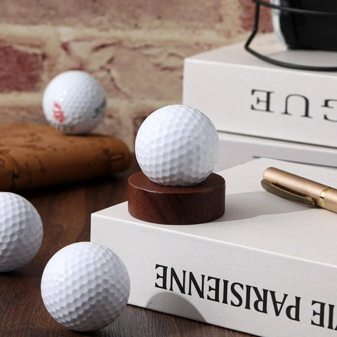 Wooden Golf Ball Display Stand For Desk With 2 Inch Ball Holder showcasing a golf ball on a tabletop with books and pen nearby.