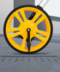 Close-up of the yellow wheel of Measuring Wheel 0-9999.9m Digital Display for Construction Worker on a measuring scale.