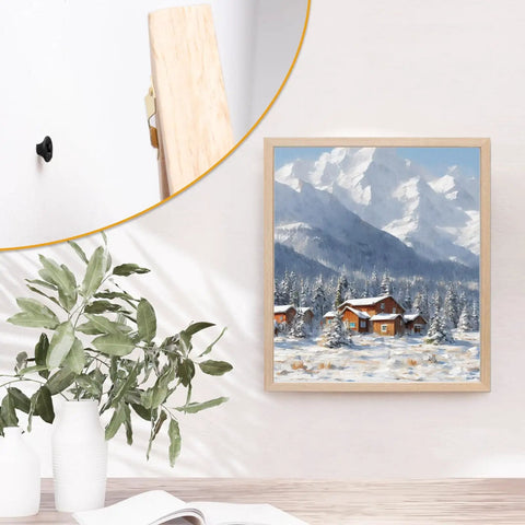 Wall-mounted painting of snowy mountain landscape with evergreen trees, framed in light wood; partial view of a black hook.