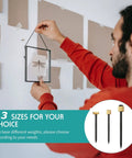 Person hanging a picture with a 75 Piece Picture Hanging Nails Set In Three Sizes Small Medium Large With Brass Head And Black Steel Finish