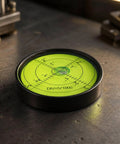 Qianly Bubble Level with Degree Markings Metal Circular Spirit Level Compact for Home Improvement Hobbyists, Turntable Alignment, Black Shell, Green Liquid, 60x12mm on a workspace.