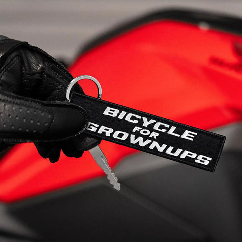 Dope Bicycle For Grownups Keychain For Riders, Pocket Sized Metal Key Ring For Motorcycles Scooters Cars And Gifts held by gloved hand