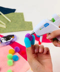 Hands using Low Temp Mini Hot Glue Gun 4 Pack White For Crafts And School Projects on colorful pom poms and felt.