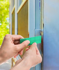 Plastic flat shim, green, installed between blue window frame and wall for leveling.