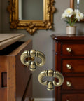 Close-up of set of 2 antique bronze ring drawer pulls with back plates on a wooden dresser in a classic room setting.