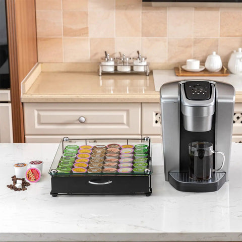 K Cup Holder Drawer with Crystal Tempered Glass Top, heavy duty metal organizer holding 42 K Cups next to a coffee maker on a counter.