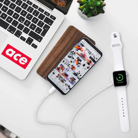 Wireless charging pad next to smartphone and smartwatch, showing 77% charge, with laptop in background, modern workspace.