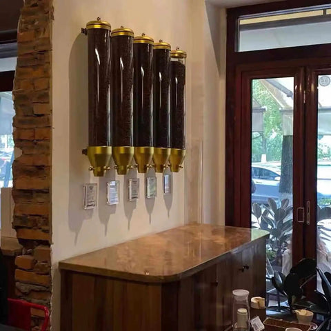 Super Heavy Duty Wall Mounted Coffee Bean Dispenser 10 Liter Airtight Gold Canisters With Clear Acrylic Front And Slam Shut Aluminum Lid For Busy Cafe Crew And Home Bars Set Of Four mounted on a wall with coffee beans inside.