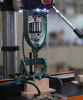 Mortising attachment in green metal mounted on a drill press with a wooden block.