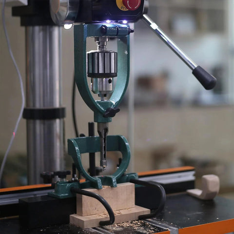 Mortising attachment in green metal mounted on a drill press with a wooden block.