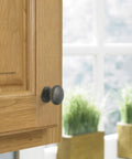 Close-up of Ravino Oil Rubbed Bronze Cabinet Knob, One And A Quarter Inch Diameter, Classic Drawer Pull on wooden kitchen cabinet.