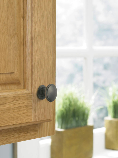 Close-up of Ravino Oil Rubbed Bronze Cabinet Knob, One And A Quarter Inch Diameter, Classic Drawer Pull on wooden kitchen cabinet.