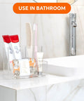 Clear Acrylic Desk Pen Holder With Three Independent Compartments used in bathroom setting, holding toiletries, on marble counter.