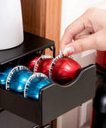 Hand accessing 4 Tier Nespresso Pod Drawer Organizer for Vertuo Capsules, holding red and blue pods in black metal drawer.