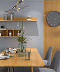 Dining area with wooden table, chairs, wall shelves, and a clock. Wall showcases oak finish similar to Dope Wood Grain Peel And Stick Wallpaper.