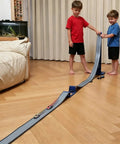 Children playing with Flexible Dual Lane Race Track With Jump Ramp Toy For Kids, 13 Feet Of Action, set up for side-by-side races indoors.