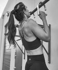 Woman using Heavy Duty Metal Resistance Band Handles With Knurled Steel Grip Surface for pull-ups on outdoor bar, back view.