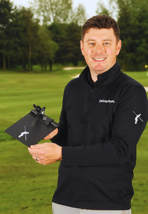 Man holding Pro Grade Golf Swing Trainer Plate With 2 Premium Gold Alignment Rods, outdoors, showing product size and use.