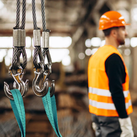 Lift sling straps: three teal 2in x 2ft polyester slings with hooks in workshop; worker in orange safety vest.