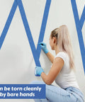 Person applying Blue Painter Tape Bulk Pack 12 Rolls 2 Inch Wide 55 Yards Each for wall painting, ensuring clean lines.