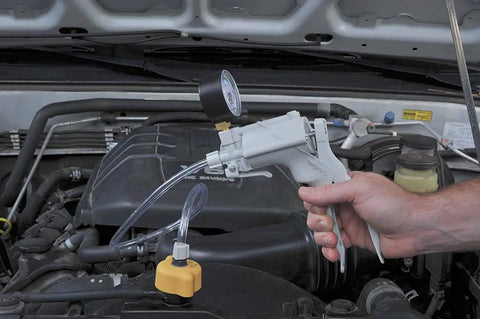 Hand holding Radiator And Cooling System Pressure Test Kit with hand pump in car engine compartment for leak detection
