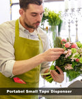 Florist in apron arranging flowers near clear noiseless packing tape with ergonomic dispenser on counter.