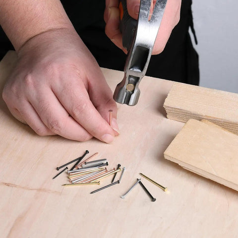 Pro Level Steel Nail Assortment Pack With 600 Pieces Across Four Different Sizes, hammering in a steel nail on wood.