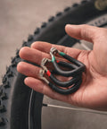 Hand holding vinyl coated bike spoke wrench with heat treated steel for 80 gauge spokes, color coded handles visible.