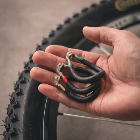 Hand holding vinyl coated bike spoke wrench with heat treated steel for 80 gauge spokes, color coded handles visible.