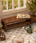 Front view of a miniature wooden bench in a dollhouse garden setup, two pack miniature wooden benches for dollhouse furniture and fairy garden decor realistic retro brown wood look perfect doll house lawn park and garden accessories totally cute collectible props.