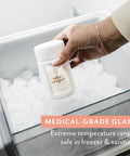 Hand holding a glass breast milk storage bottle in ice, showcasing the Ultra Wide Neck Glass Breast Milk Storage Bottles For Pumping And Feeding Bpa Free Silicone Caps Fit Most Pumps Aspen White Pair For Busy Mommas Keeping Fresh Stashes On Deck.