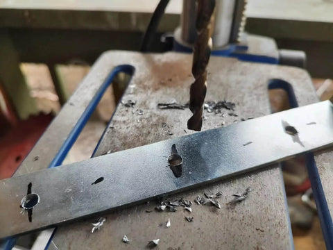Close-up of a cobalt drill bit drilling into a metal strip on a workbench with metal shavings.