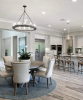 Modern open kitchen and dining area with round table, white chairs, and pendant lights over an island in elegant white decor.