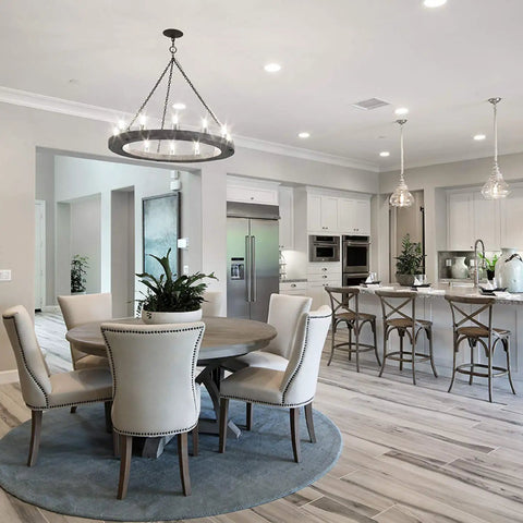 Modern open kitchen and dining area with round table, white chairs, and pendant lights over an island in elegant white decor.