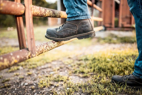 Person wearing Women Work Boots 6 Inch Steel Toe Brown Wide 7 D Built For Tough Shifts Slip Resistant Rubber EVA Treker Outsole stepping on a rusty gate