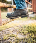 Person wearing Women's Steel Toe Work Boot 6 Inch Brown Wide 10D Built Tough Leather Construction With Slip Resistant Treker Outsole Meets ASTM F2413-18 EH SR FIC And F3445-21 Safety Standards, stepping on a rusty gate.