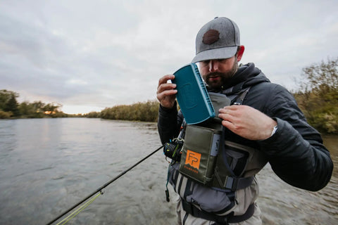 Angler adjusting Stormshadow Fly Fishing Chest Pack With Waterproof Pocket by river, highlighting tool attachment in use.